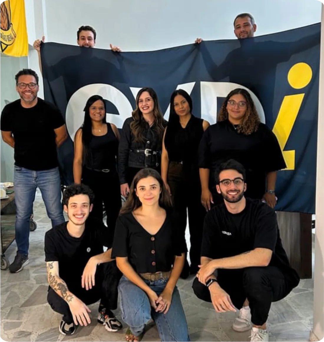 Time da Exdi reunido em frente à bandeira da agência
